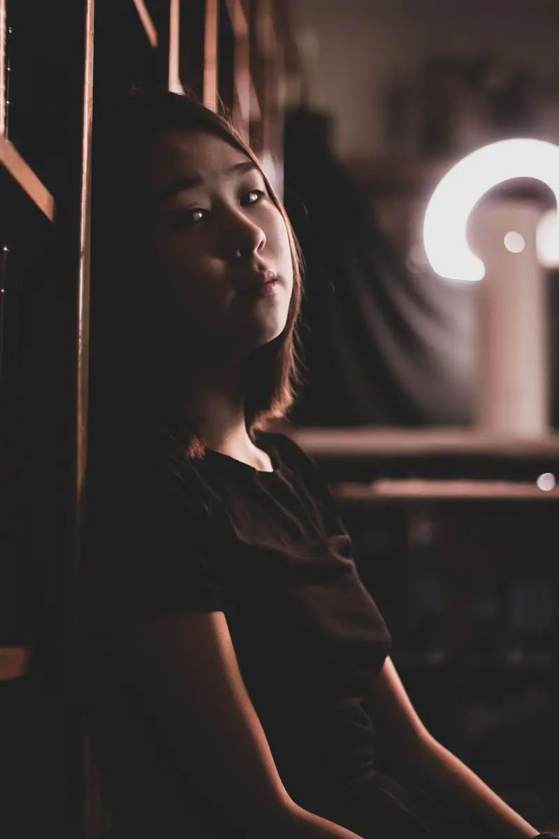 A woman leaning against a bookshelf in dim light
