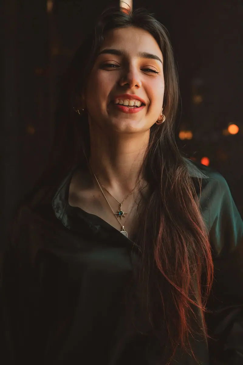 A smiling woman with long hair in a dark room with warm light